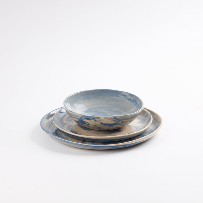 Three piece handmade ceramic dinner set with a marbled clay pattern in cobalt blue, beige and cream on a white background by Palinopsia
