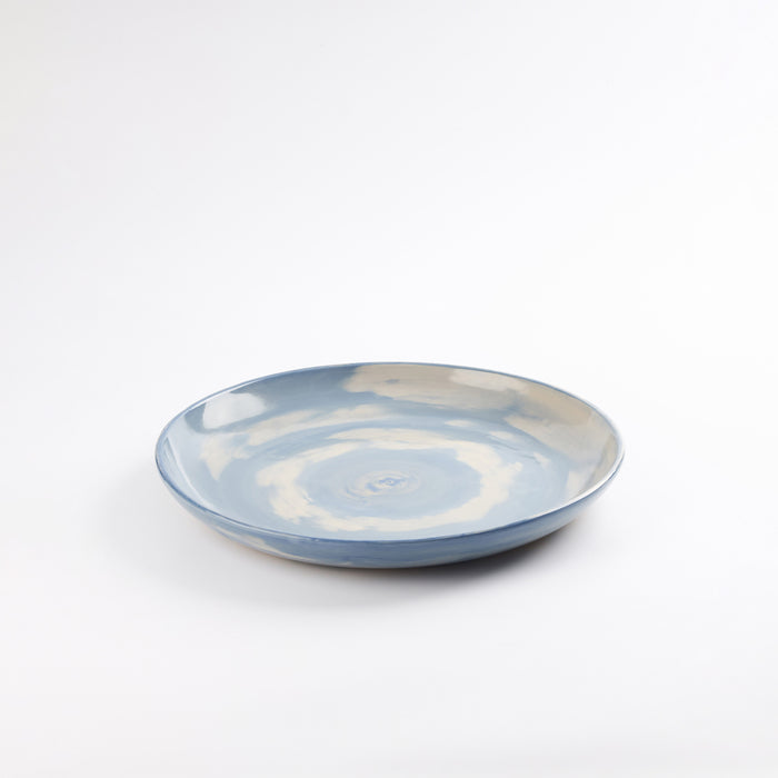 Handmade ceramic dinner plate with a swirling marbled clay pattern in cobalt blue, beige and cream on a white background by Palinopsia