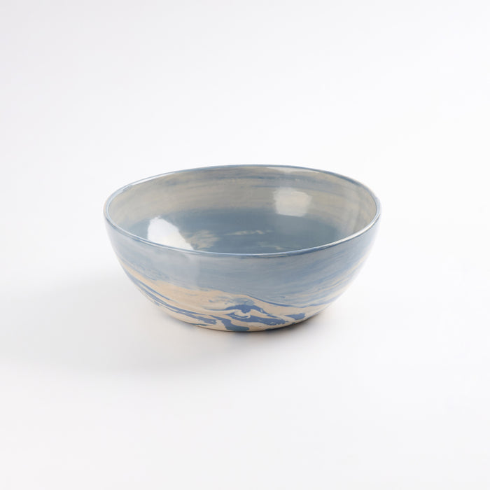 Handmade ceramic bowl with a swirling marbled clay pattern in cobalt blue, beige and cream on a white background by Palinopsia