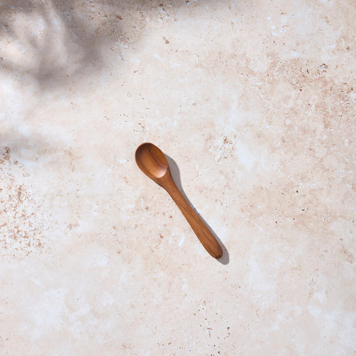 Bird’s-eye view of a Palinopsia small wooden teak spoon on a light stone background.