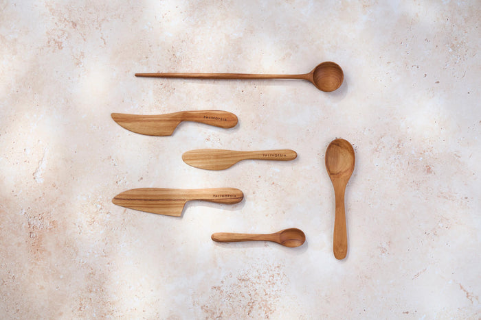 A variety of Palinopsia teak wooden spoons and knives of different shapes and sizes on a light stone background.