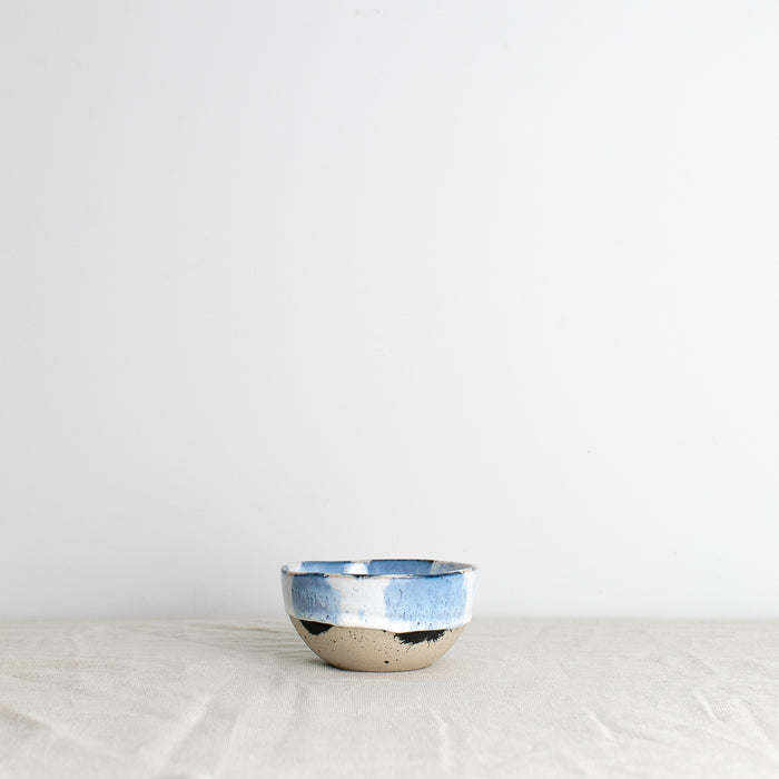 Handmade blue and white little breakfast bowl with splatter design on a white tablecloth by Palinopsia Ceramics
