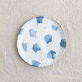 Bird's-eye view of a single Palinopsia's Dinner Plate in the coastal Pollock collection, with blue and white splatters and drippy glaze on a linen tablecloth