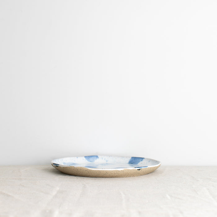 A single handmade Palinopsia dinner plate in blue and white splatter design with drippy glaze, on a white background