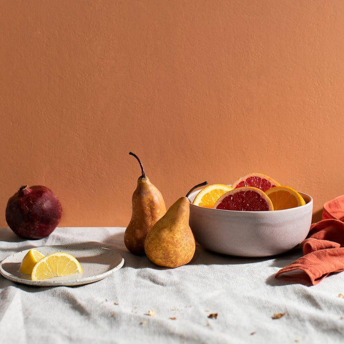 Side view of a summer table with bright orange background showing handmade ceramics by Palinopsia Ceramics and bright summer fruits
