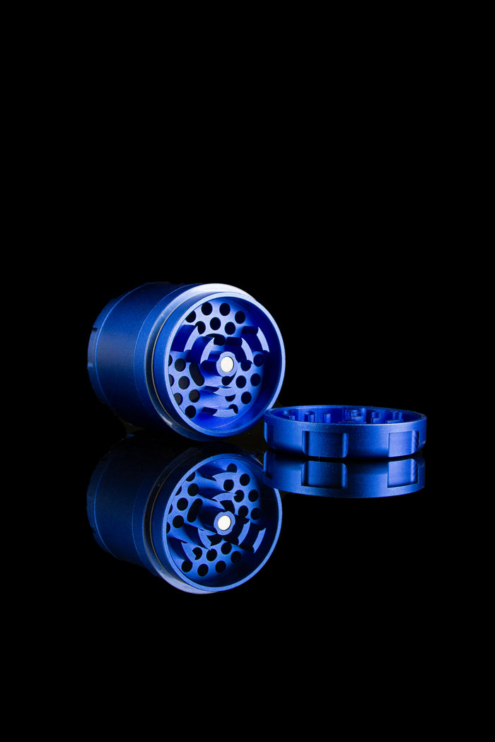 Blue cannabis grinder with open components reflected on a dark surface.