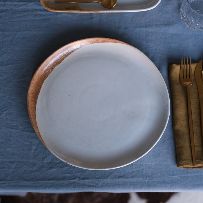 Birds-eye view of a handmade dinner plate in blue and brown on blue linen tablecloth by Palinopsia Ceramics