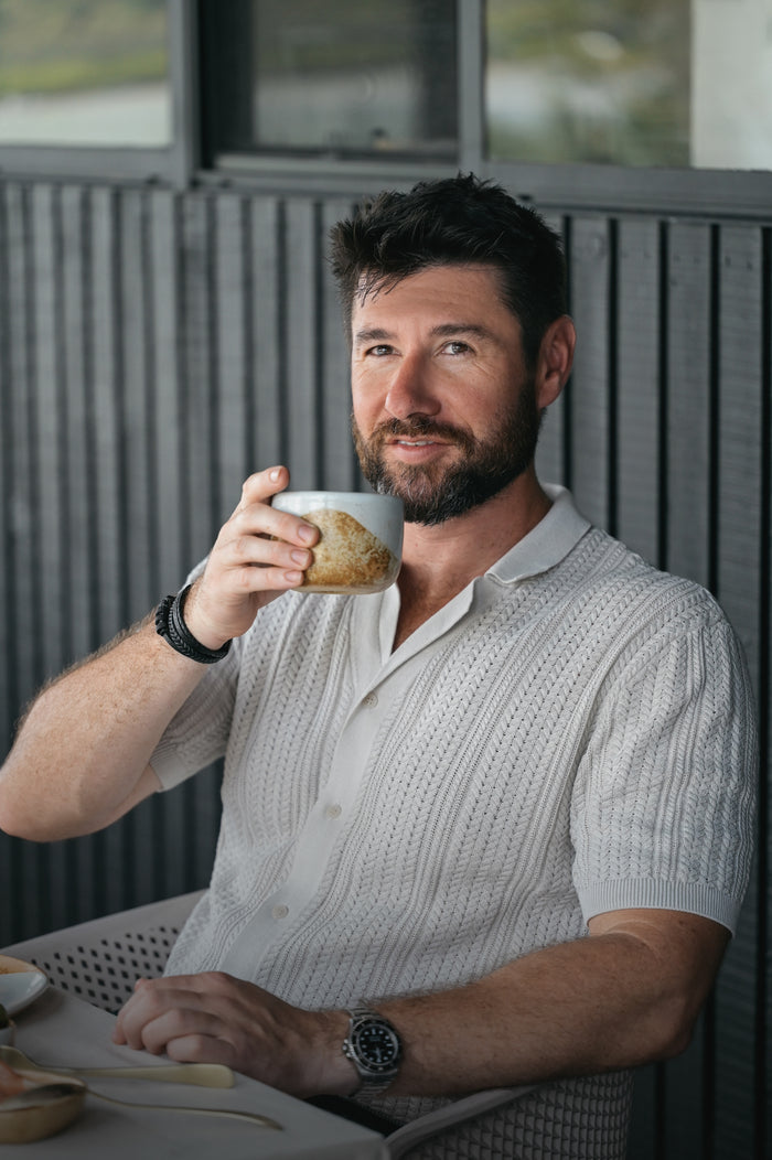 Man drinking from a Palinopsia ceramic cup outdoors with a blurred weatherboard house background