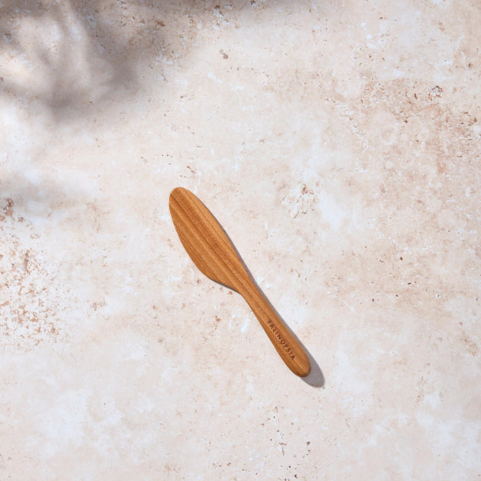 Bird’s-eye view of a Palinopsia wooden teak spreading knife on a light stone background.