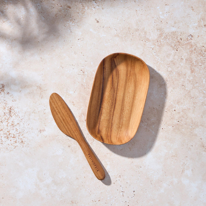 Bird’s-eye view of a Palinopsia teak wooden serving tray and knife on a light stone background.