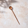 Bird’s-eye view of a Palinopsia long wooden teak spoon on a light stone background.
