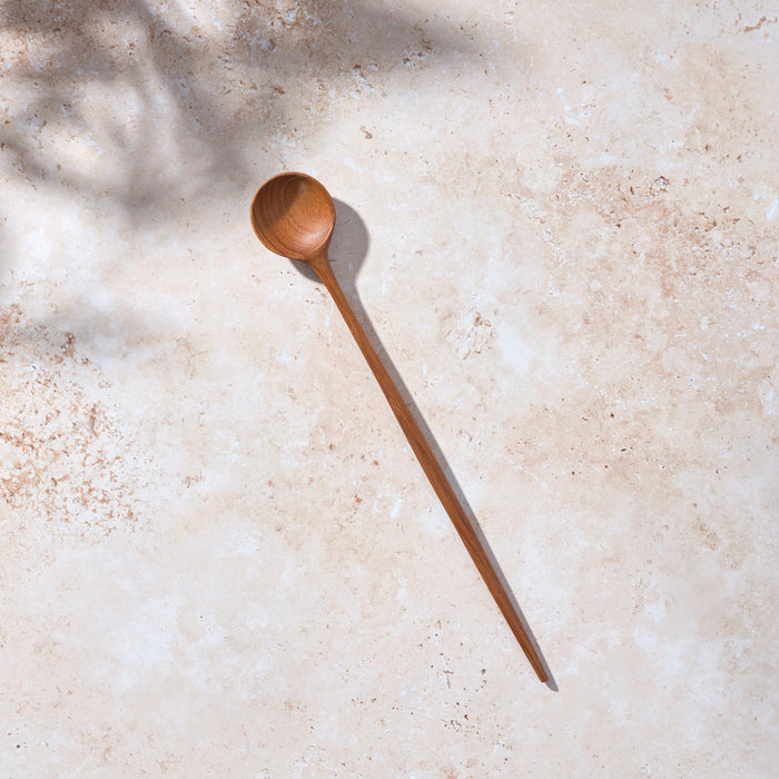 Bird’s-eye view of a Palinopsia long wooden teak spoon on a light stone background.