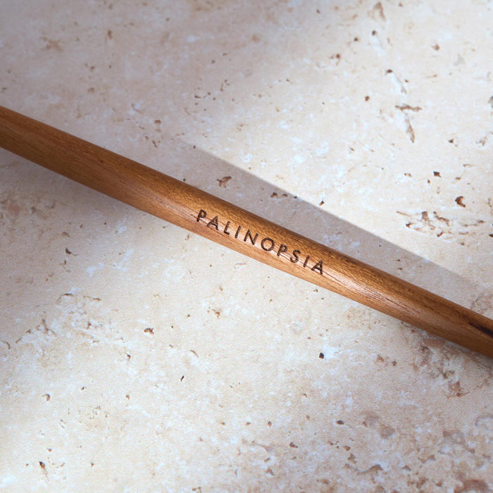 Close-up shot of the handle of a teak wooden stirring spoon with a Palinopsia label on the handle.