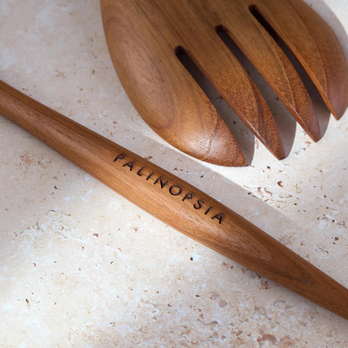 Close-up shot of teak wooden salad servers with Palinopsia labels on the handle.