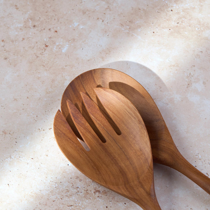 Detailed shot of a large teak wooden salad serving set by Palinopsia on a light stone background.