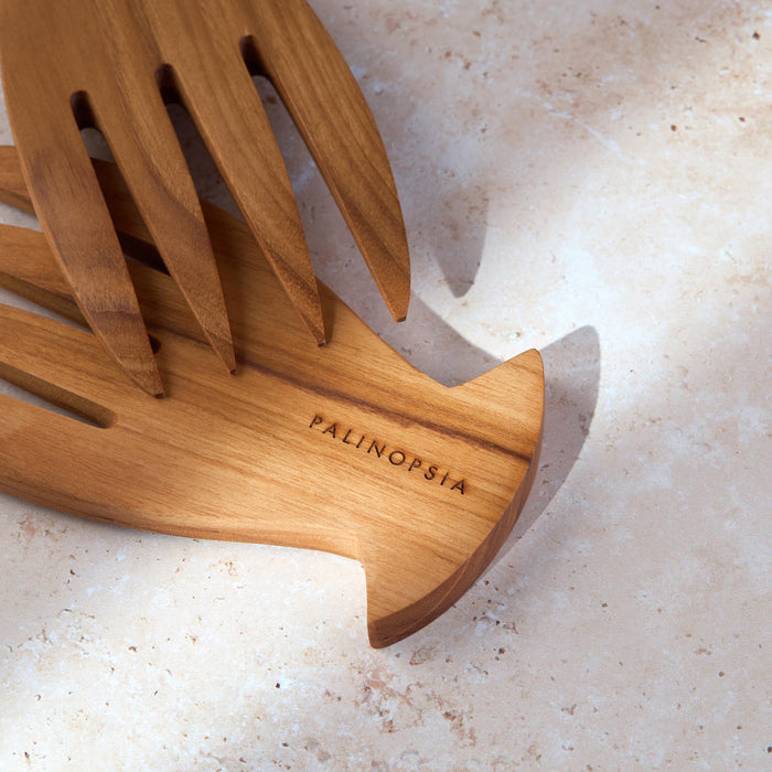 Close-up shot of a teak wooden salad serving set with the Palinopsia label on a light stone background.