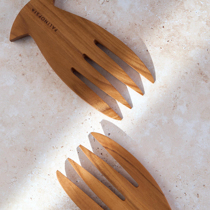 Detailed shot of a teak wooden salad serving forks by Palinopsia on a light stone background.
